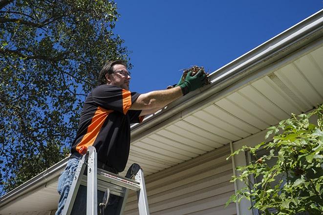 worker repairing damaged gutter on a residential roof in Cayuga